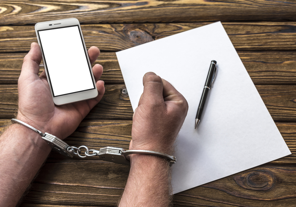 Person with handcuffs and holding mobile phone