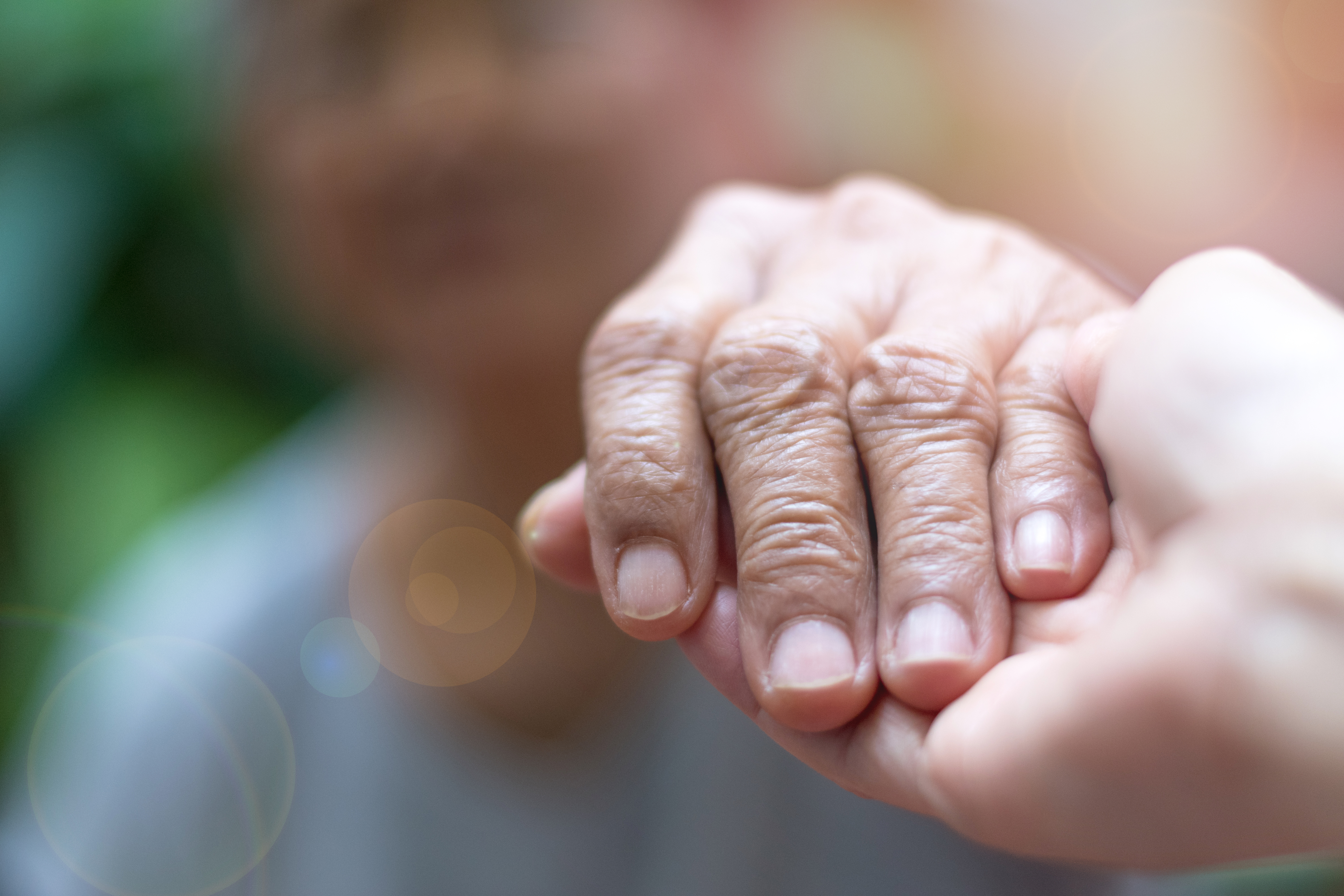 Elderly woman holds carer's hand