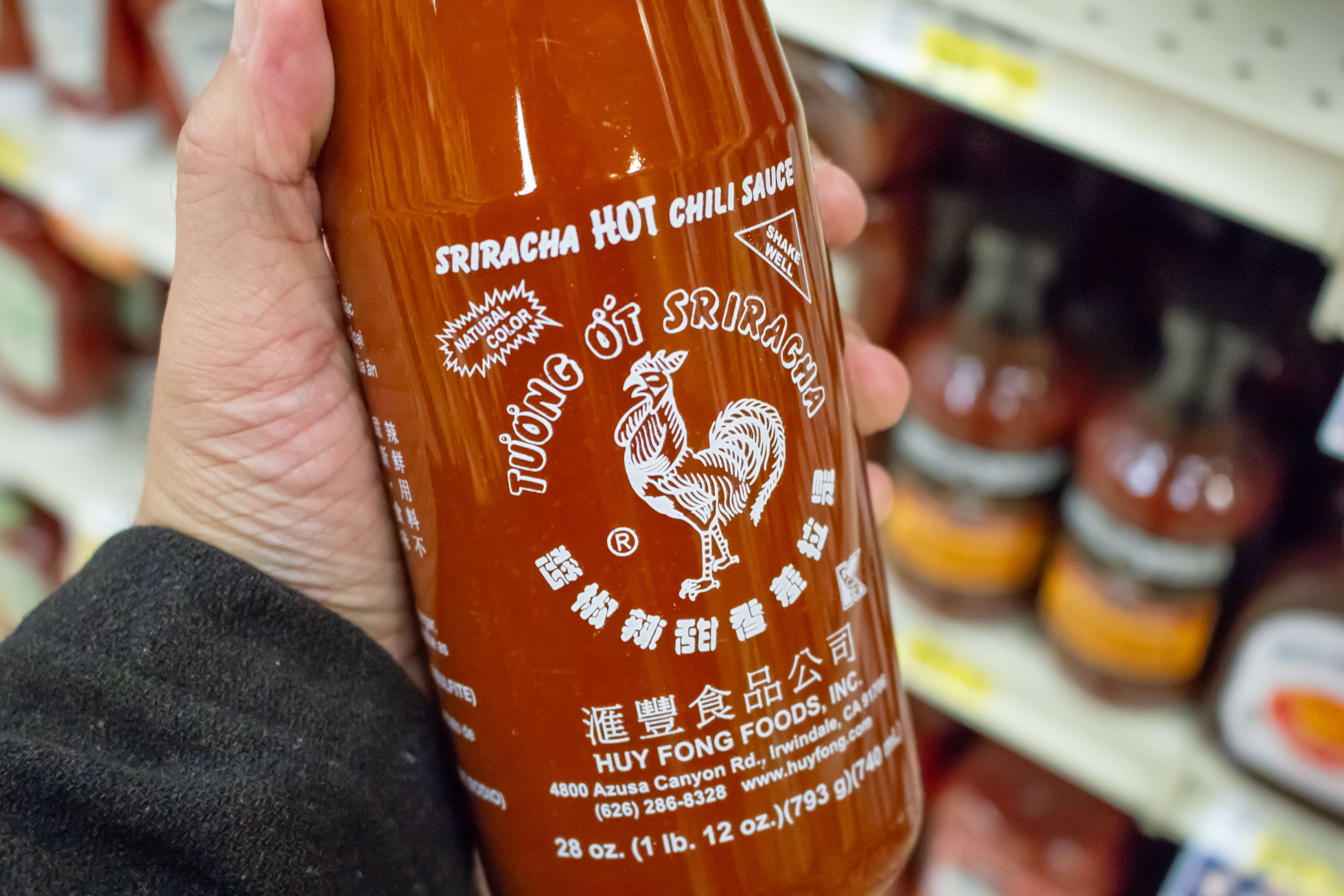 Hand holding a Sriracha chilli sauce bottle